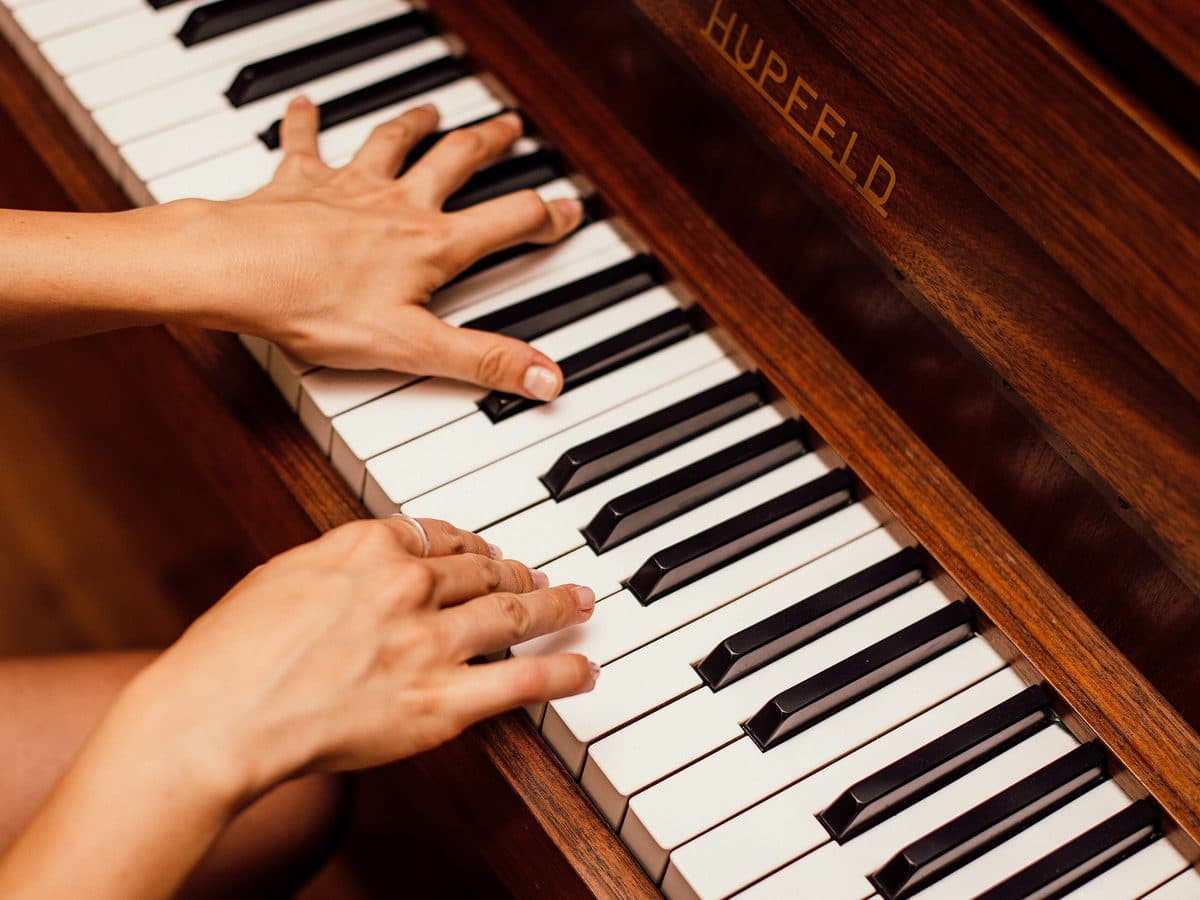 Dues mans tocant el teclat d’un piano de fusta.